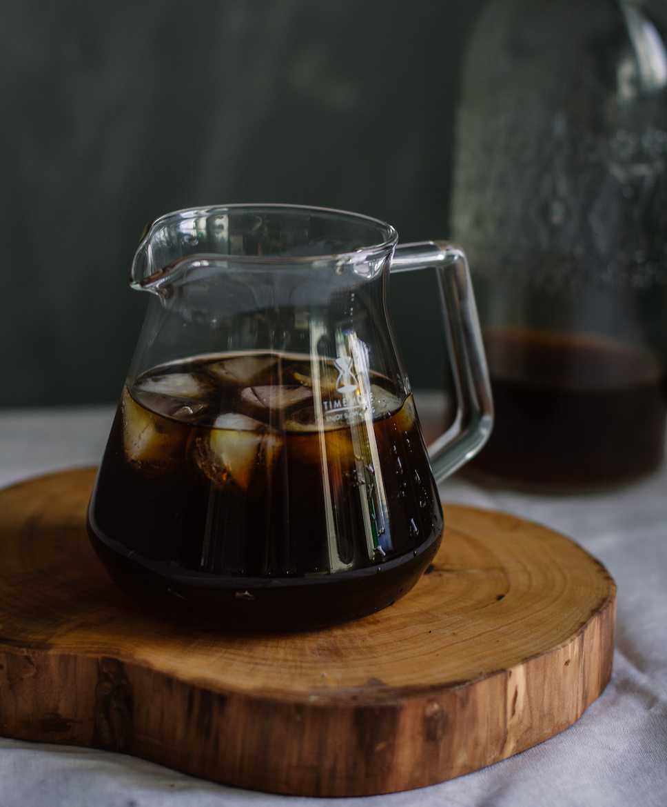 Cold brew coffee in a pitcher with ice on a wood tray